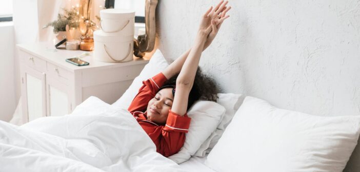 Frau in rotem Pyjama, die im Bett liegt und die Arme in die Höhe streckt.