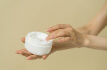 Hände, die einen Cremetiegel halten und mit den Fingern in die Creme eintauchen