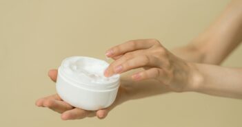 Hände, die einen Cremetiegel halten und mit den Fingern in die Creme eintauchen